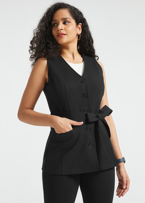 Woman wearing black button-front ponte vest with V-neckline, tie waist and hand in front pocket