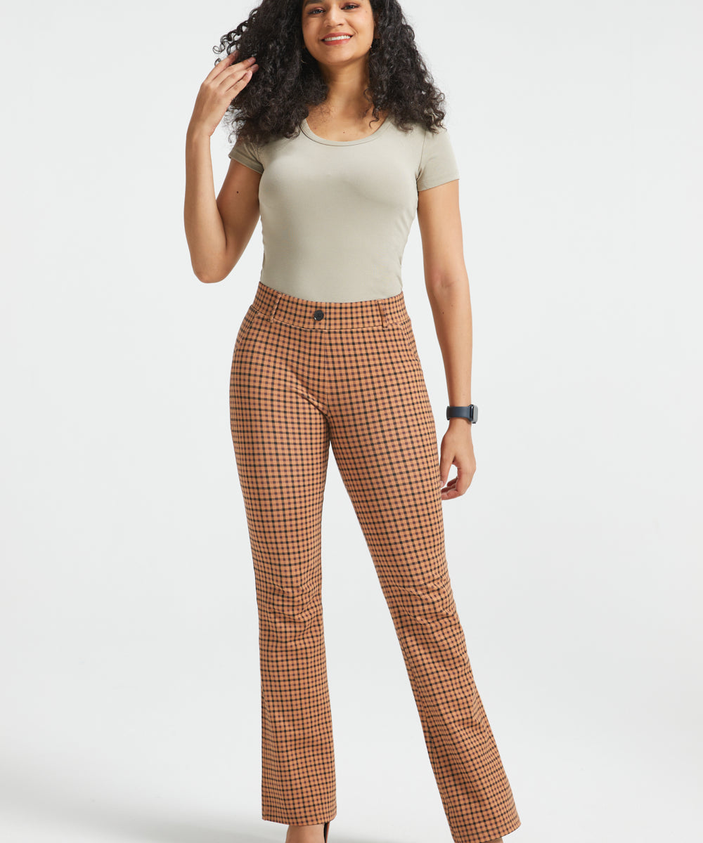 A woman modeling brown and beige checkered flared trousers, standing against a light gray studio background.