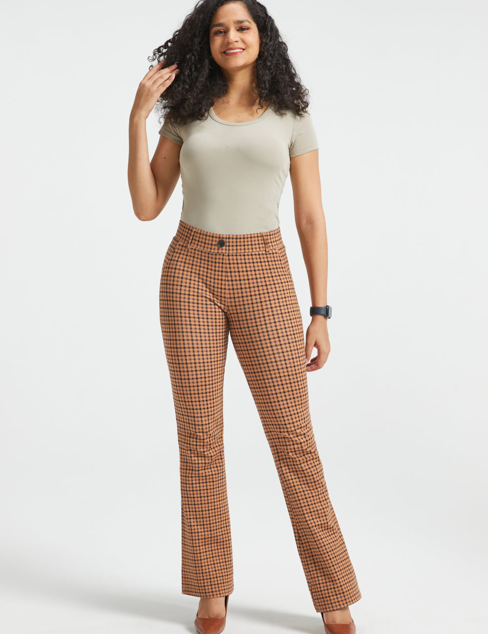 A woman modeling brown and beige checkered flared trousers, standing against a light gray studio background.